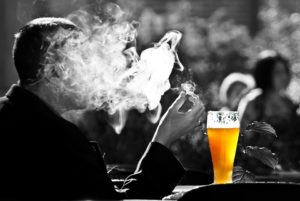 man smoking with a beer in front of him